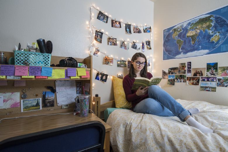 A student reads a book while sitting on the bed of her dorm room in the UWC-USA school