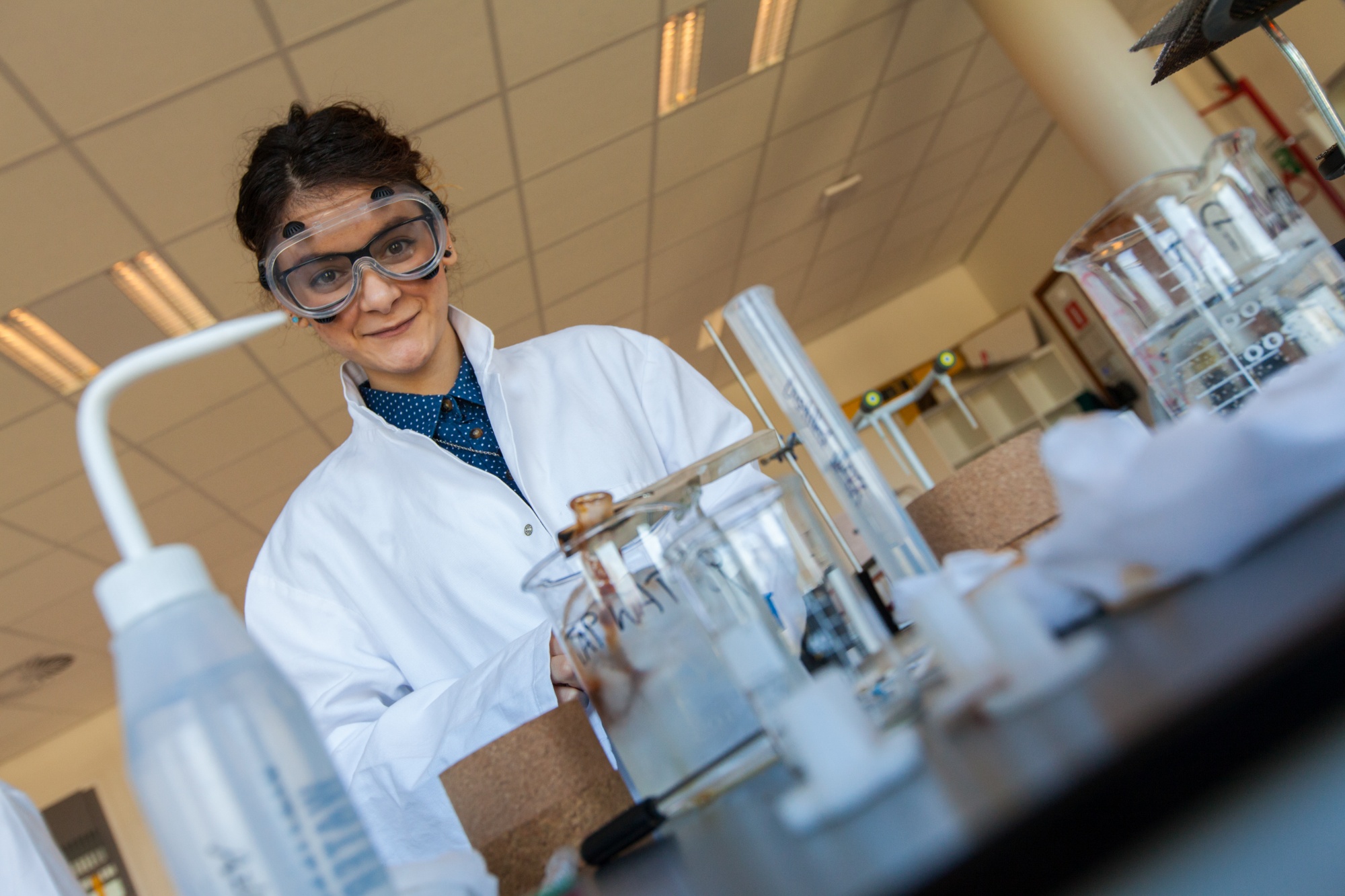 A young female student in lab coat enjoys working on an experiment