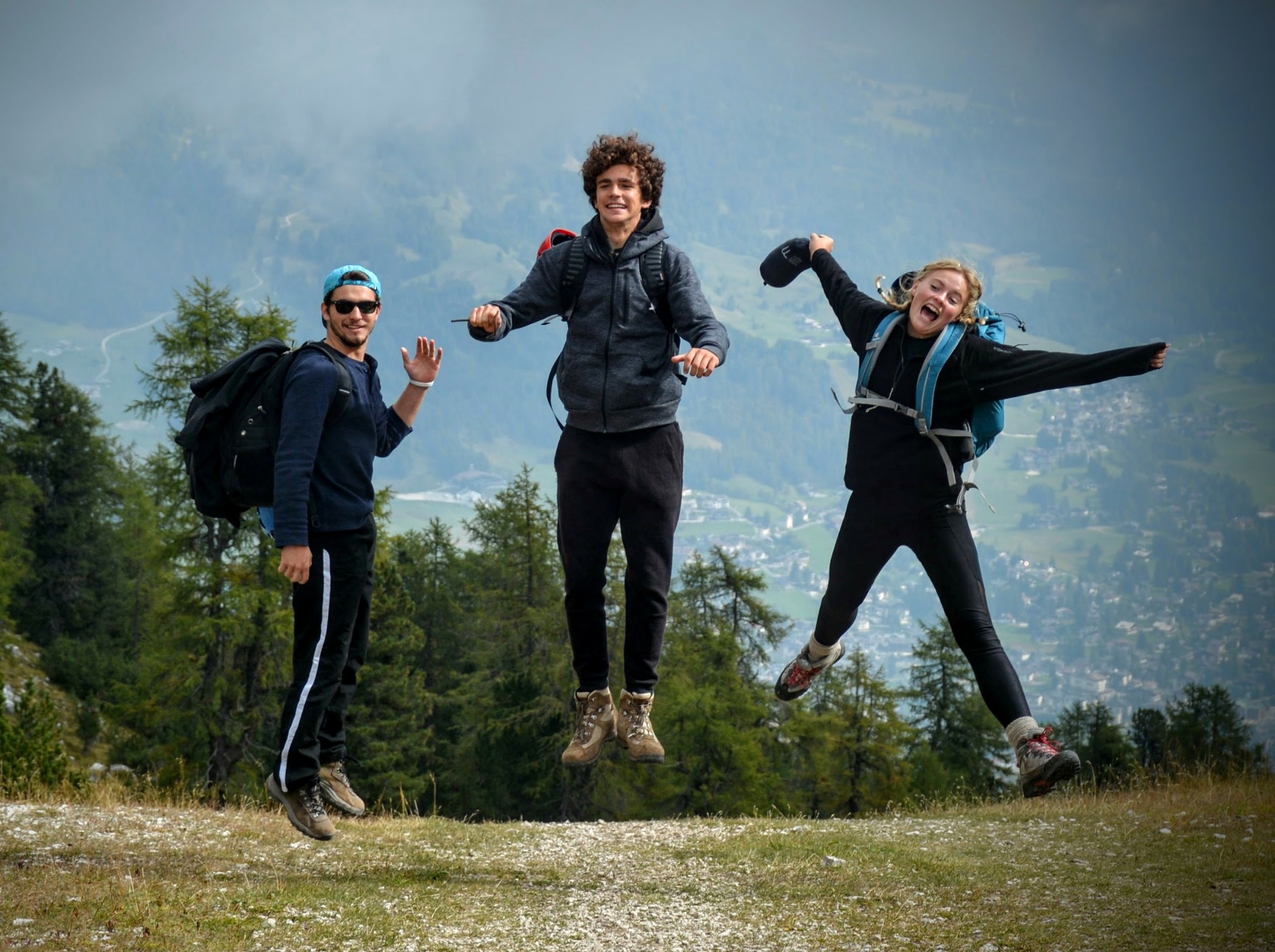 Three UWC students jump for joy as they reach the top of a mountain.