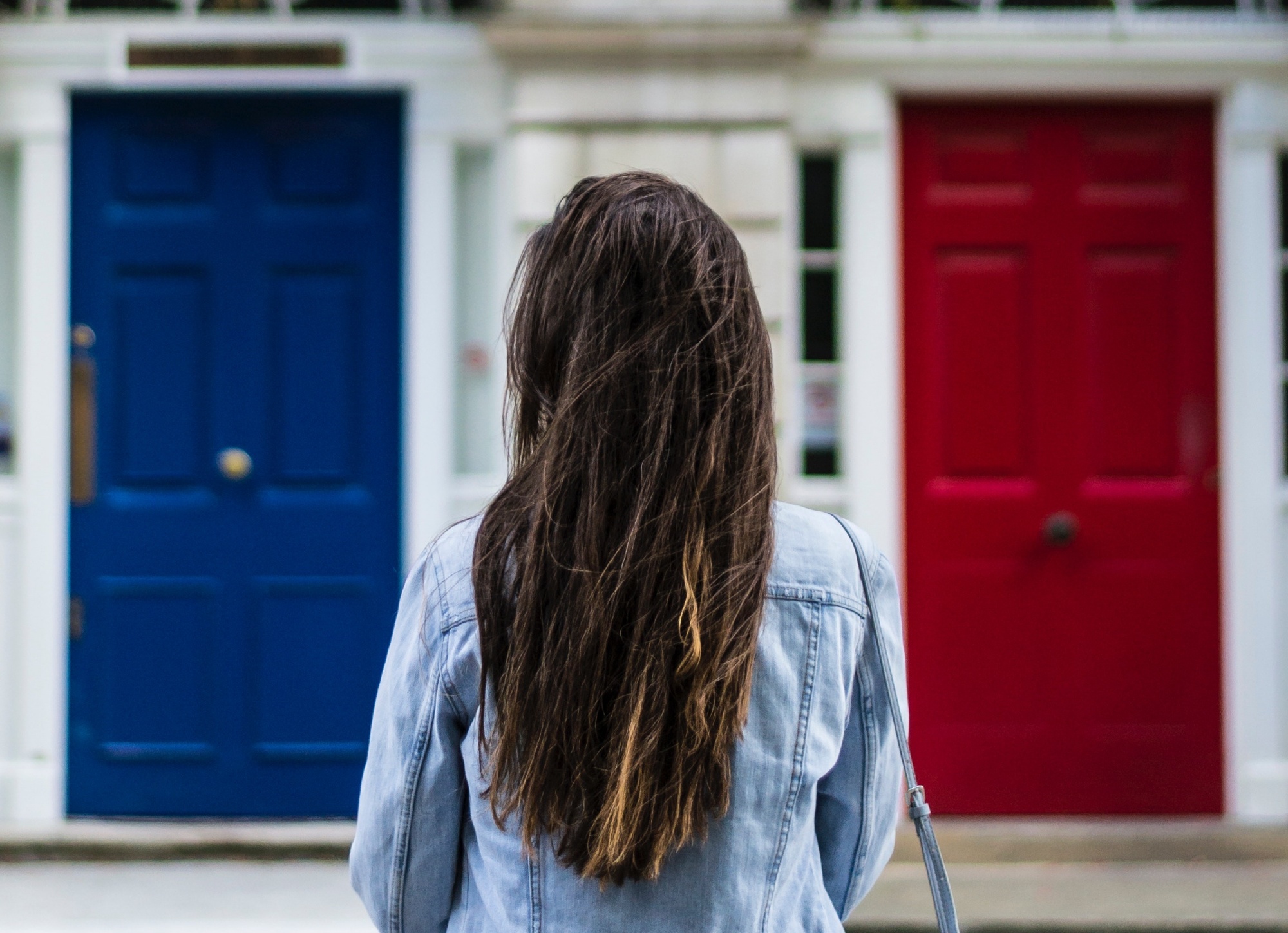 A young lady with brown hair faces a choice of two doors she can enter through.